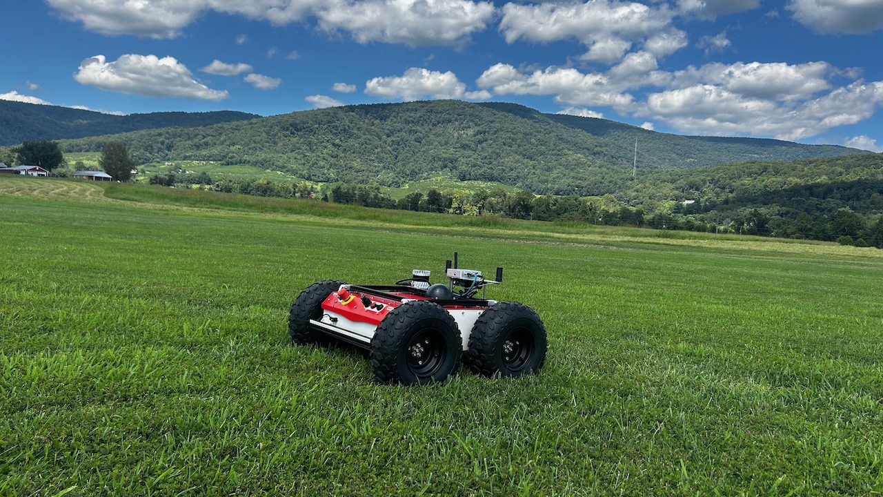A robotic vehicle with four large rubber tires on a grassy field, with rolling hills behind it